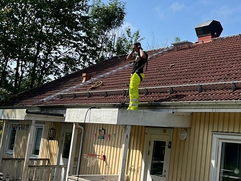 Tegeltak på ett radhus med mörk beläggning och mossa, med en person i varselkläder på taket under arbetet